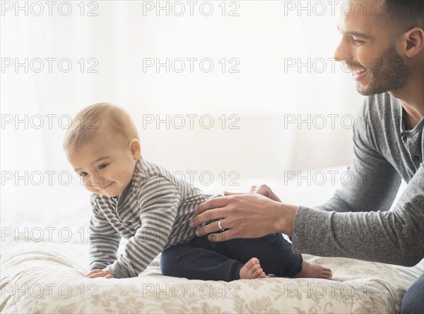 Father playing with baby son on bed