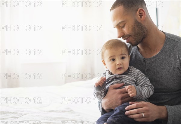 Smiling father holding baby son on bed