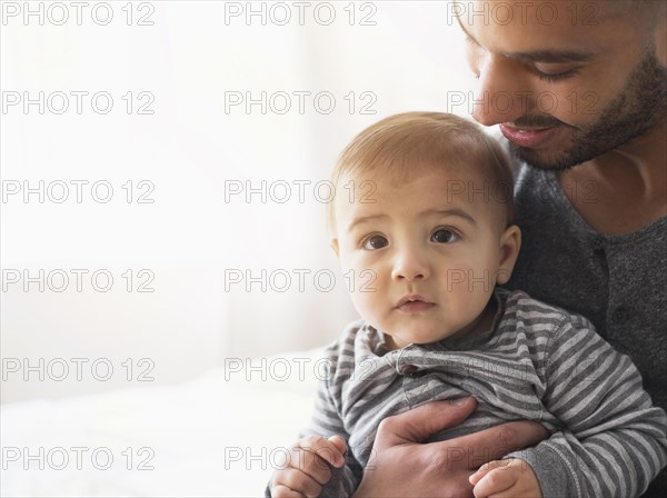 Smiling father holding baby son on bed