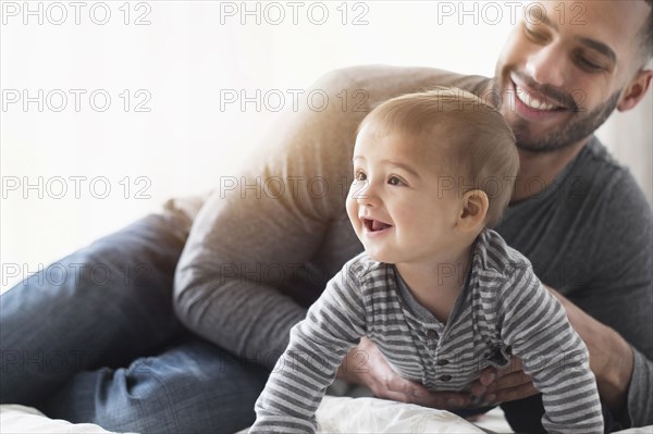 Smiling father playing with baby son on bed