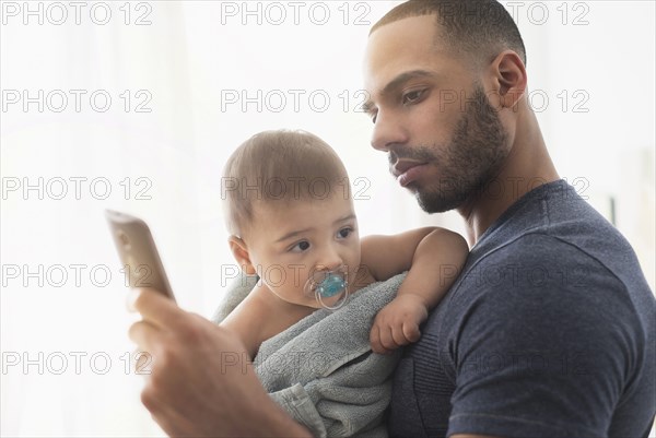 Father holding baby son and using cell phone