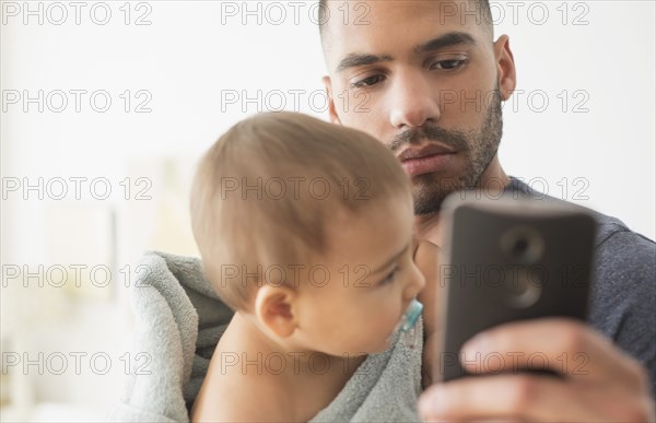 Father holding baby son and using cell phone
