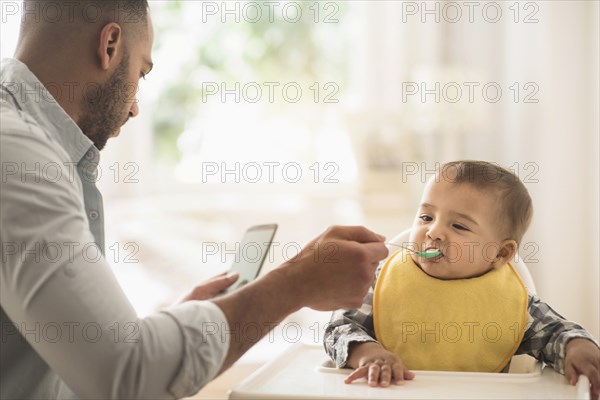 Father texting on cell phone and feeding baby son