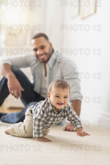 Father watching baby son crawling on floor