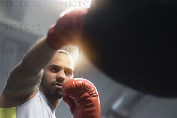 Close up of Hispanic man punching bag in gym