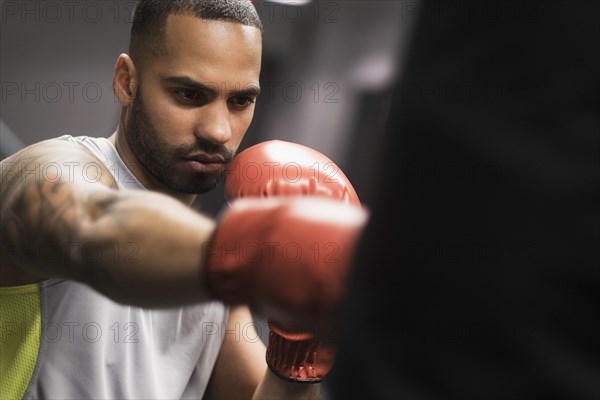 Close up of Hispanic man punching bag in gym