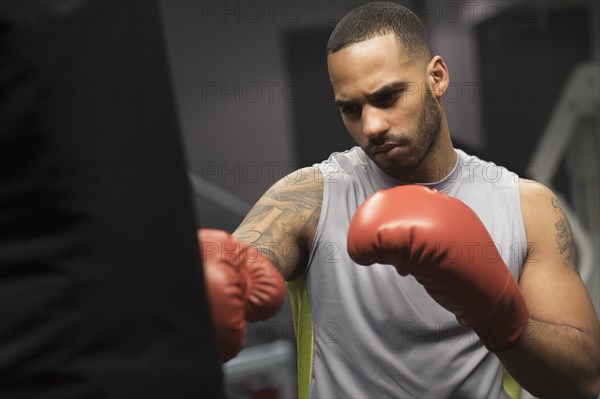 Close up of Hispanic man punching bag in gym