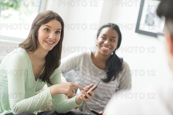 Smiling woman pointing to cell phone with friends