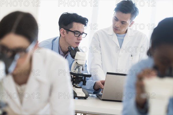 Scientists using microscopes and laptop in research laboratory