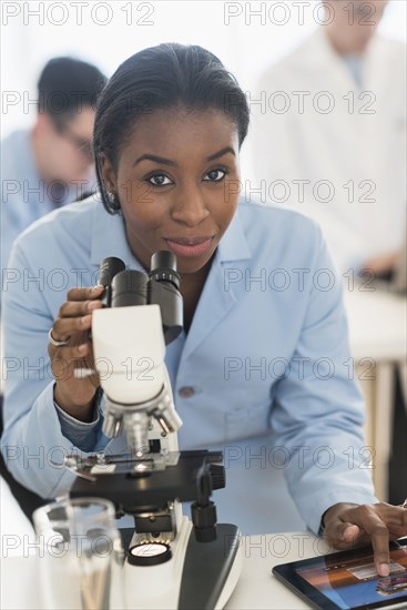 Scientist using microscope and digital tablet in research laboratory