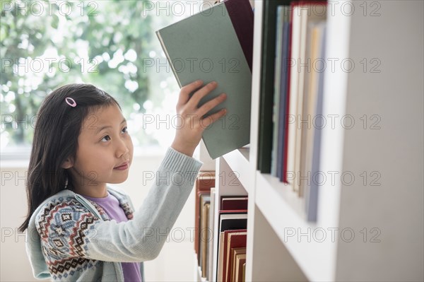 Chinese student selecting book from library bookcase