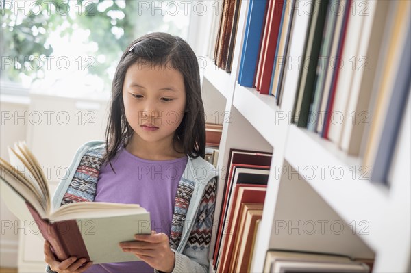 Chinese student reading book near library bookcase