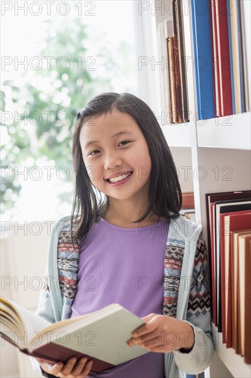 Chinese student reading book near library bookcase