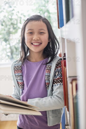 Chinese student reading book near library bookcase