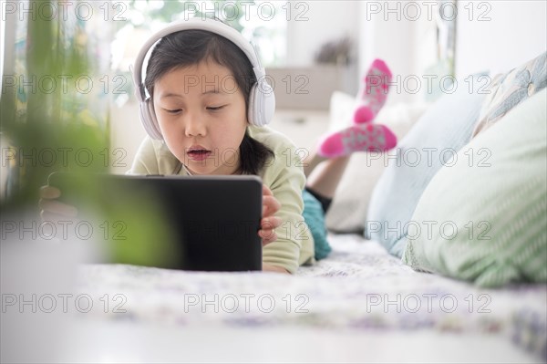 Chinese girl using digital tablet with headphones on bed