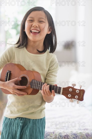 Chinese girl practicing ukulele in bedroom