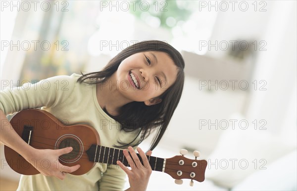 Chinese girl practicing ukulele in bedroom