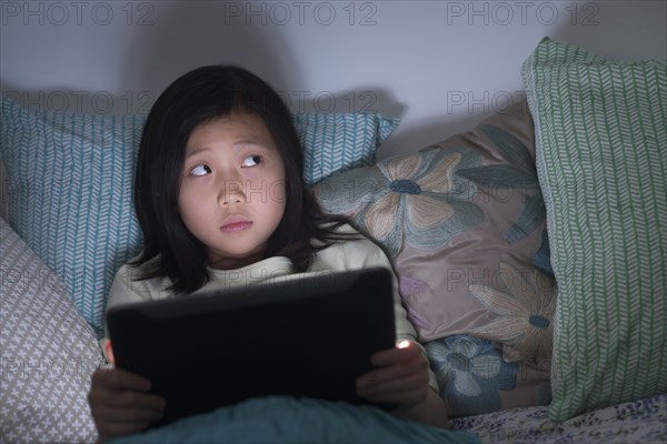Nervous Chinese girl watching digital tablet in bed