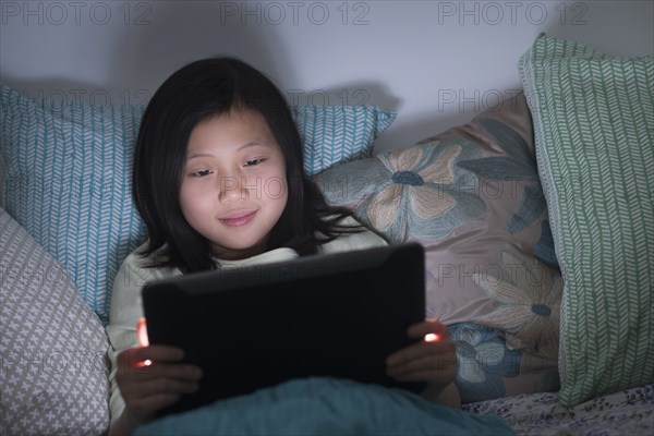 Smiling Chinese girl watching digital tablet in bed