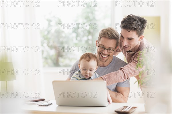Caucasian gay fathers and baby using laptop