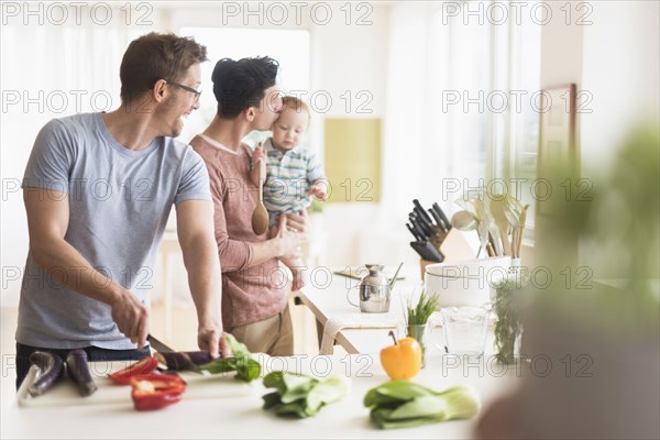 Caucasian gay fathers and baby cooking in kitchen