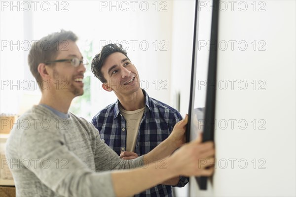 Caucasian gay couple hanging picture on wall
