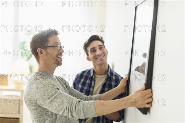 Caucasian gay couple hanging picture on wall