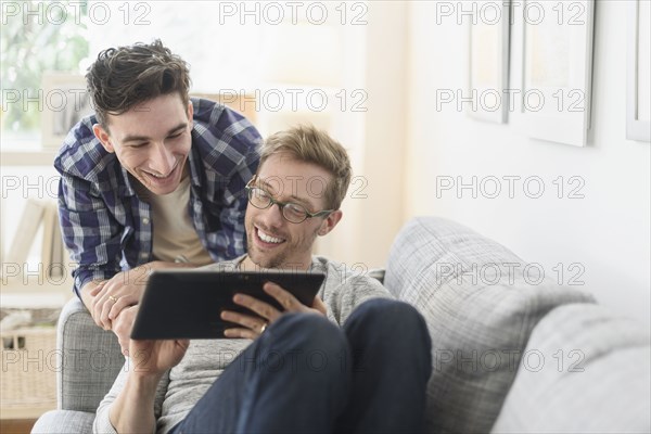 Caucasian gay couple using digital tablet on sofa