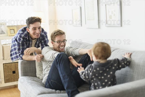 Caucasian gay fathers and baby relaxing on sofa