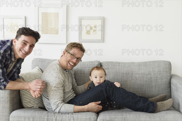 Caucasian gay fathers and baby relaxing on sofa