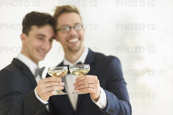 Caucasian gay grooms toasting with champagne at wedding