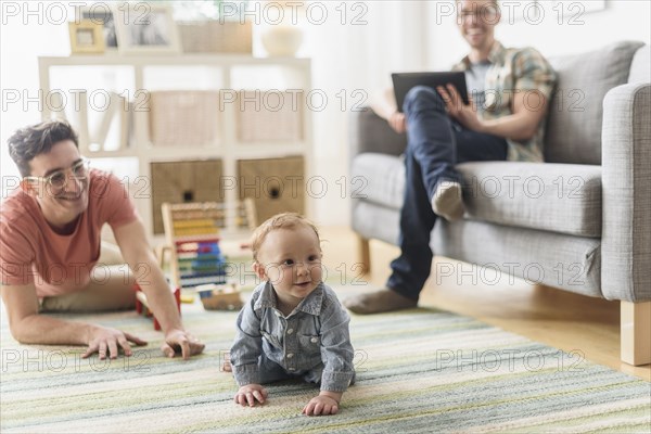 Caucasian gay fathers and baby relaxing in living room