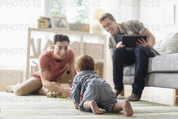 Caucasian gay fathers and baby relaxing in living room