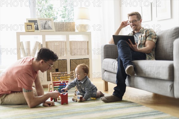 Caucasian gay fathers and baby relaxing in living room