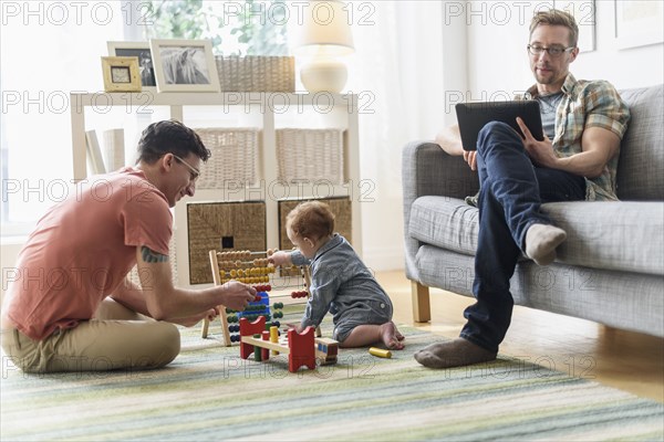 Caucasian gay fathers and baby relaxing in living room