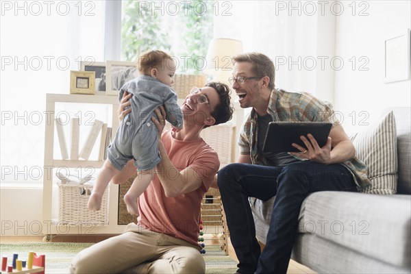 Caucasian gay fathers and baby relaxing in living room