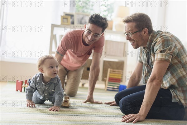 Caucasian gay fathers and baby playing in living room