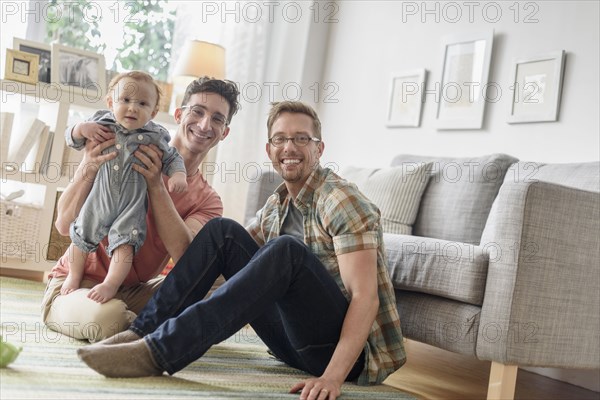 Caucasian gay fathers and baby playing in living room
