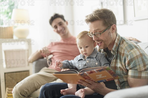 Caucasian gay fathers reading to baby in living room