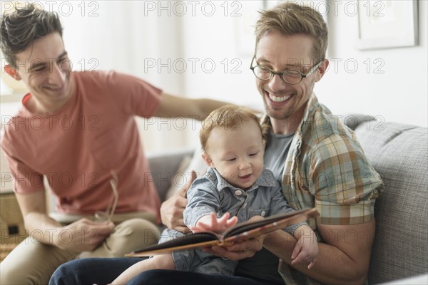 Caucasian gay fathers reading to baby in living room