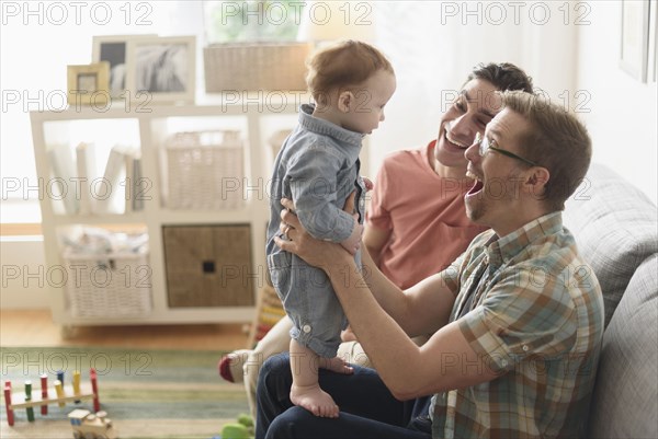 Caucasian gay fathers and baby playing in living room