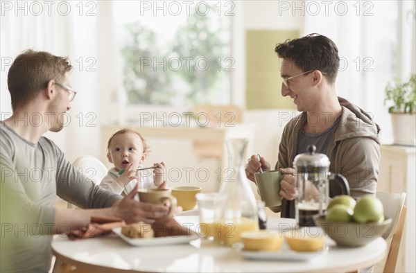 Caucasian gay fathers and baby eating breakfast