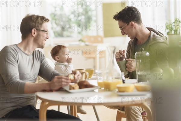 Caucasian gay fathers and baby eating breakfast
