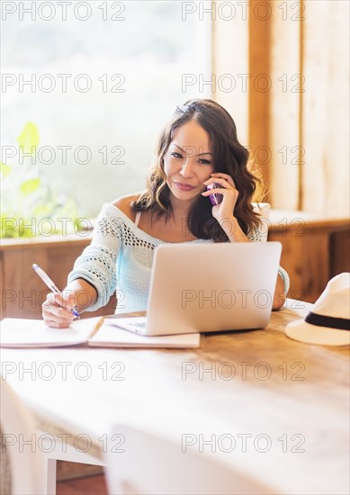 Chinese woman on cell phone using laptop in cafe