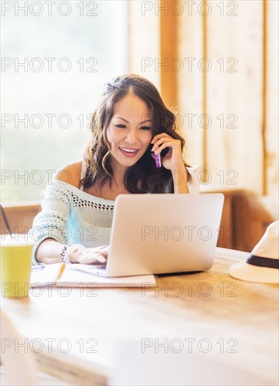 Chinese woman on cell phone using laptop in cafe