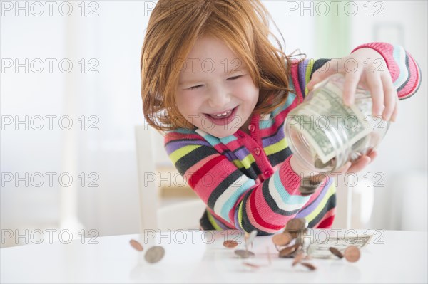 Caucasian girl pouring money from change jar