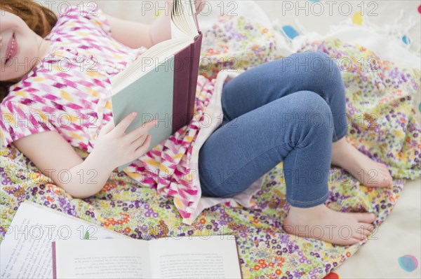 Caucasian girl reading book on bed