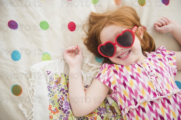 Caucasian girl wearing heart -shaped sunglasses on bed