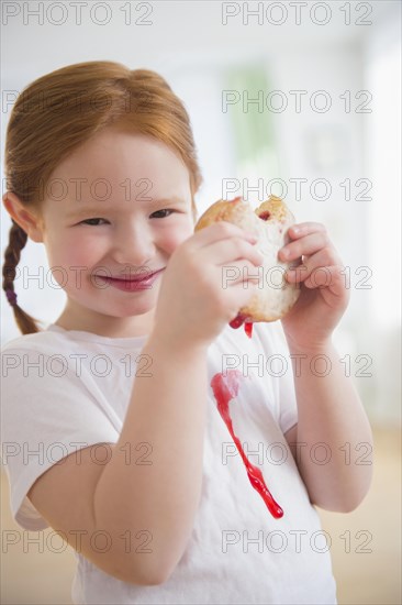 Caucasian girl eating messy jelly donut