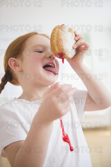 Caucasian girl licking messy jelly donut